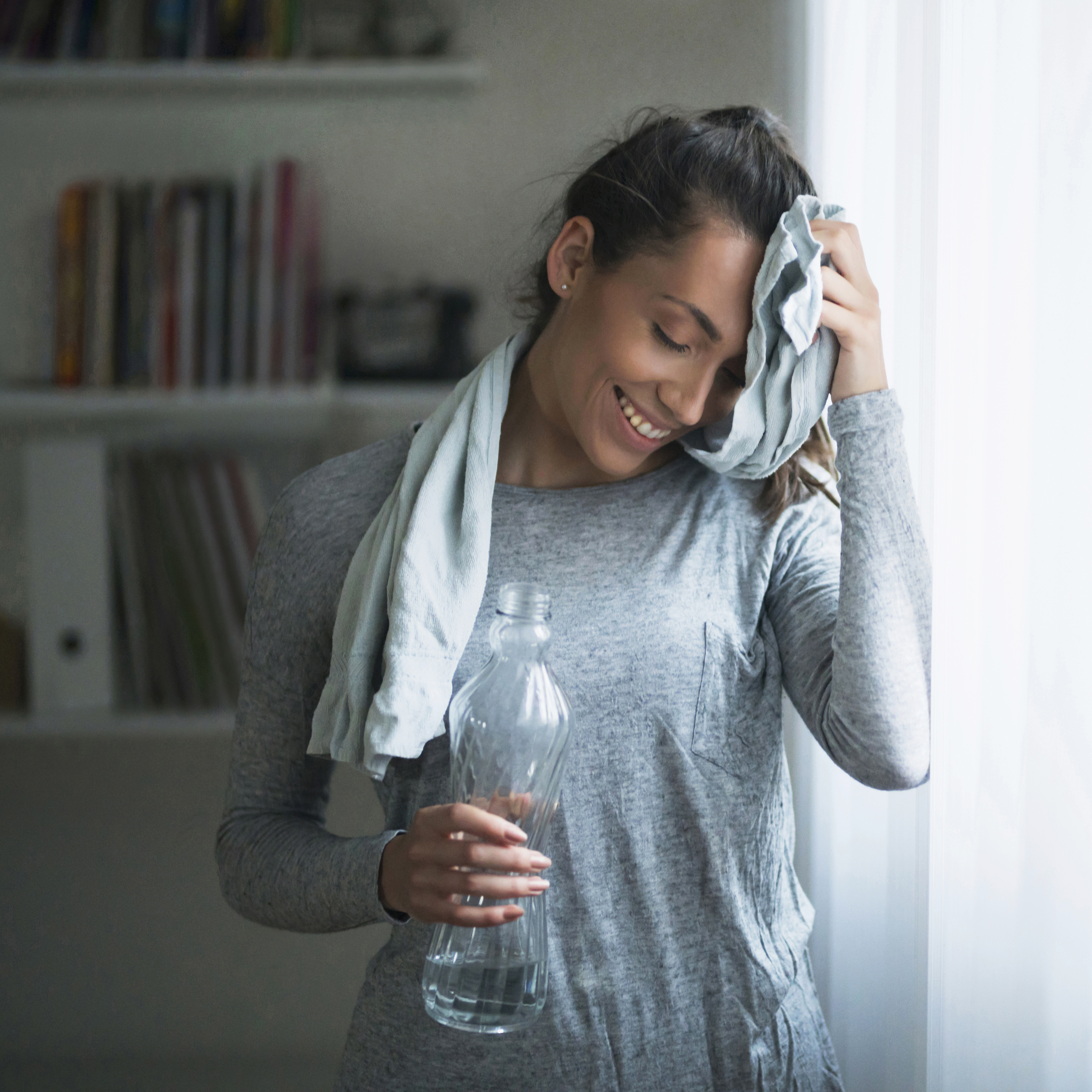 一位微笑的妇女在家中锻炼后用毛巾擦去额头上的汗水