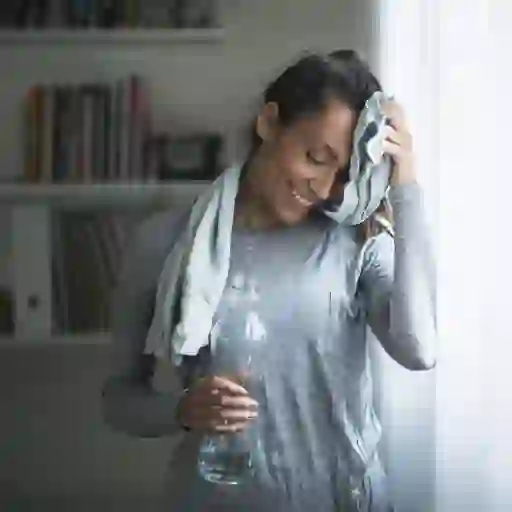一位微笑的妇女在家中锻炼后用毛巾擦去额头上的汗水