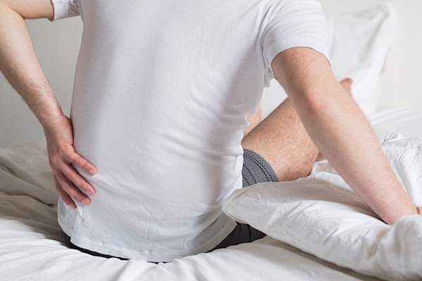 男子坐骨神经痛坐起来在床上。