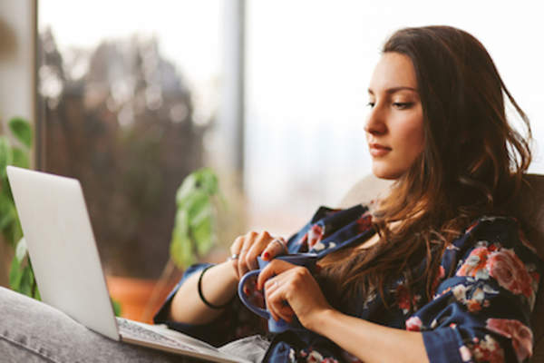 坐在椅子上用笔记本电脑阅读,手里拿着咖啡。