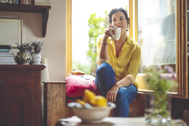 一位中年妇女坐在她家厨房的柜台上喝咖啡。