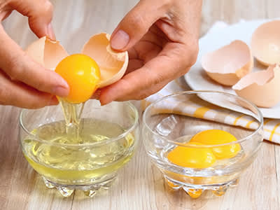 女人的手打破鸡蛋，把蛋清和蛋黄分开。