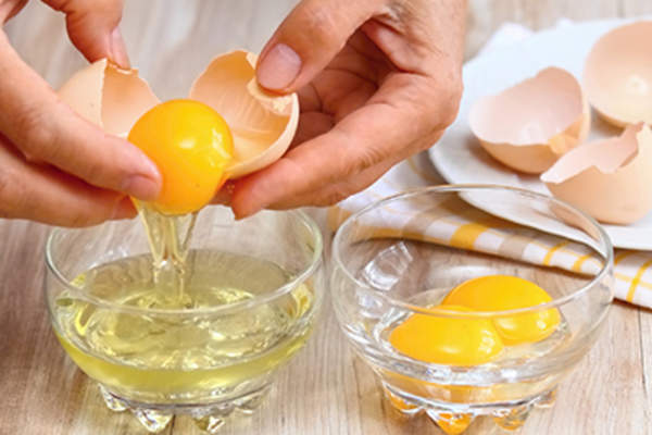 女人的手打破鸡蛋,把蛋清和蛋黄分开。