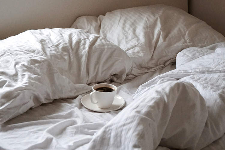 在未整理的床上喝一杯热咖啡。