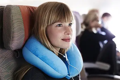 使用脖子枕头的微笑的妇女在飞机上。