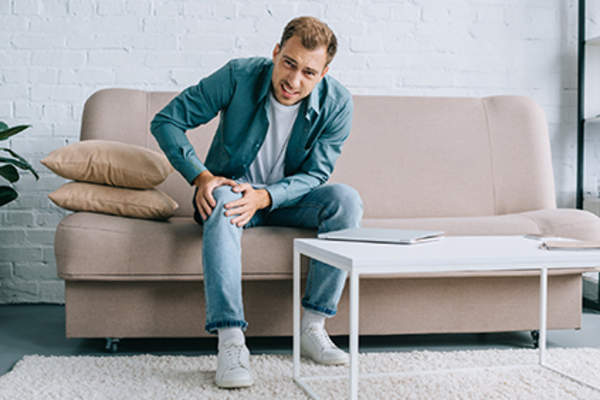 Man on the couch has joint pain from a rheumatoid arthritis flare.
