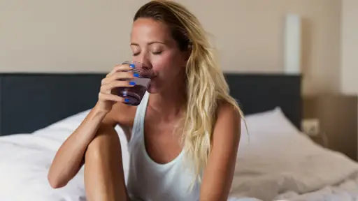 一个年轻的女人坐在床上喝着一杯水。