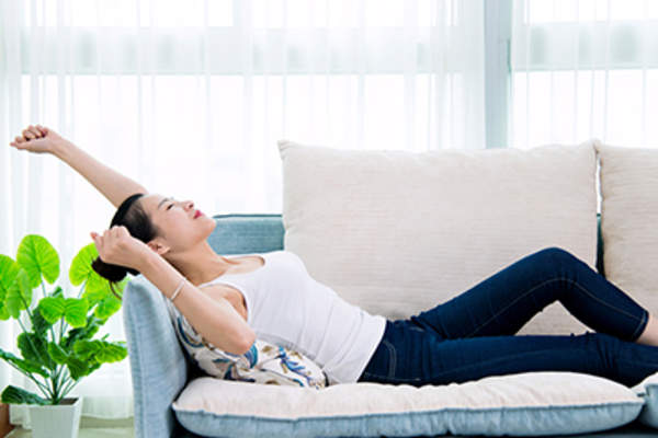 年轻女子在家里的沙发上伸展身体。