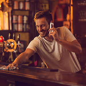 微笑的酒保在工作时用手机。