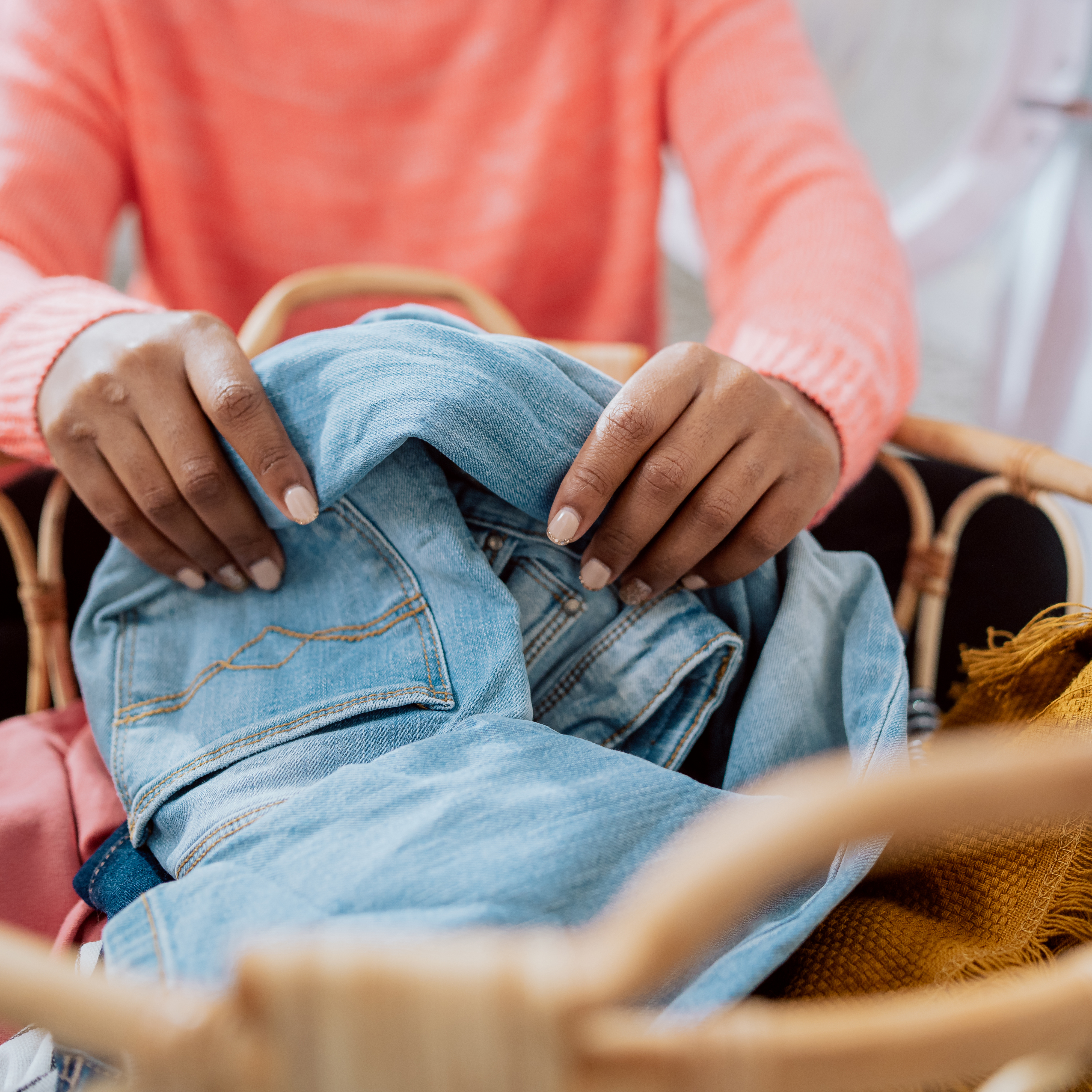 特写:一个女人的手坐在洗衣房的地板上，把柳条篮子里的衣服分类，把东西扔进洗衣机的滚筒，