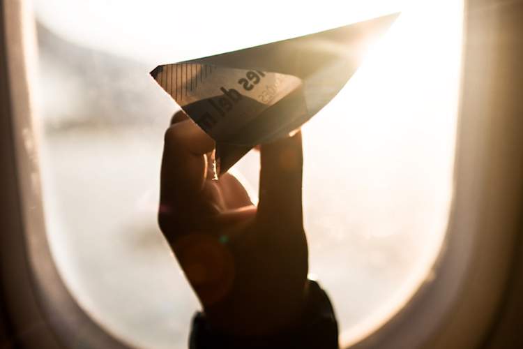 在飞机窗口前手拿着纸飞机