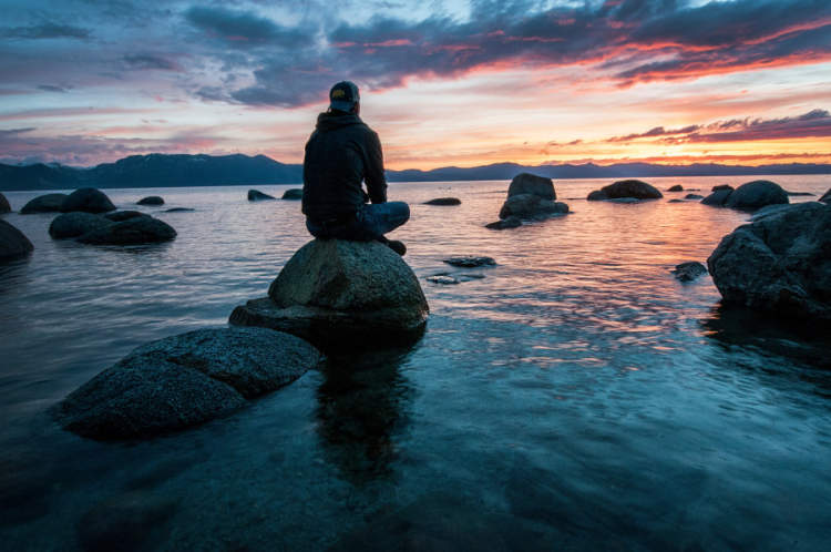 一名男子坐在水中的岩石上冥想