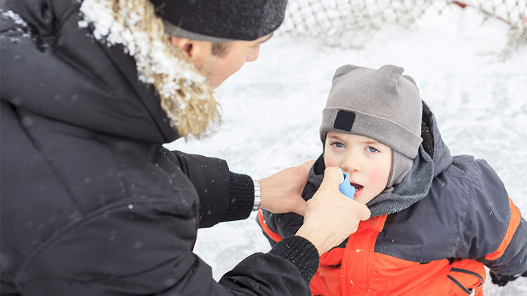 爸爸帮助年幼的儿子患有哮喘使用吸入外面的冬天。