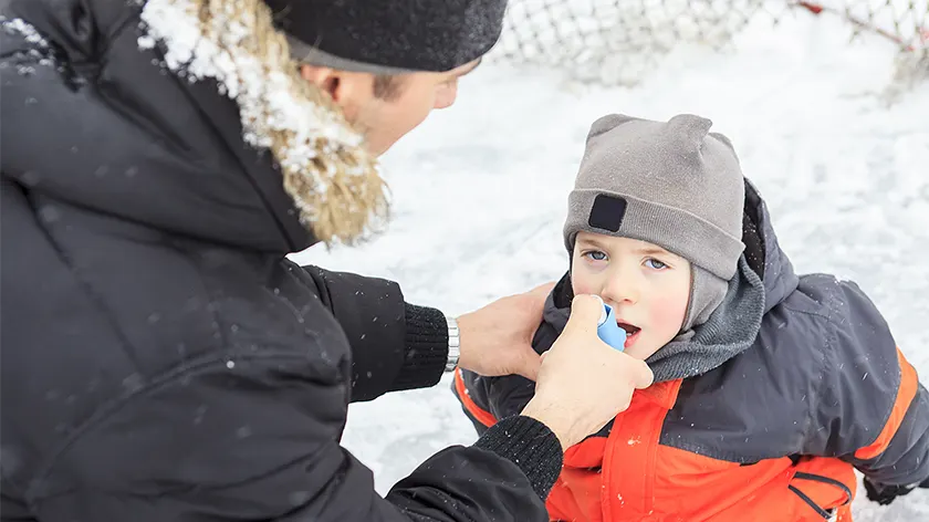 爸爸在冬天帮助患有哮喘的儿子在户外使用吸入器。