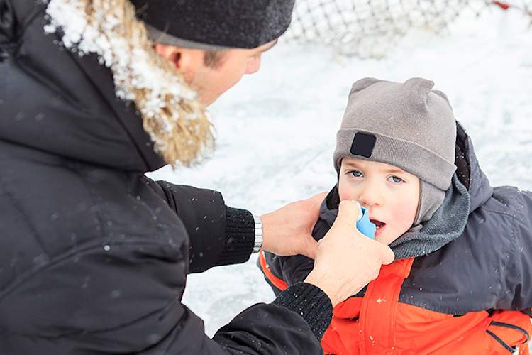 爸爸帮助年幼的儿子患有哮喘使用吸入外面的冬天。