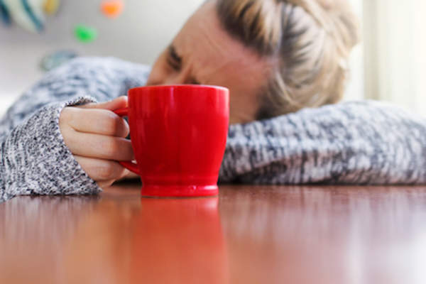 疲惫的女人头靠在桌子上,端着一杯咖啡。