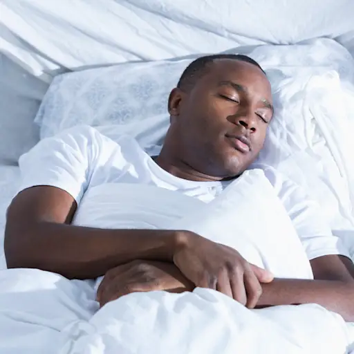 Young African American man asleep on back in bed.
