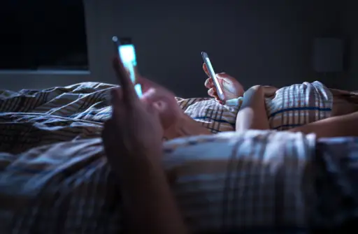couple in bed at night looking at phones