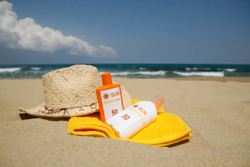 Sun block cream and spray on towel with beach hat.