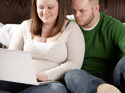 超重的年轻夫妇看着床上的笔记本电脑。