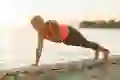 A woman does a shoulder tap in plank position outside