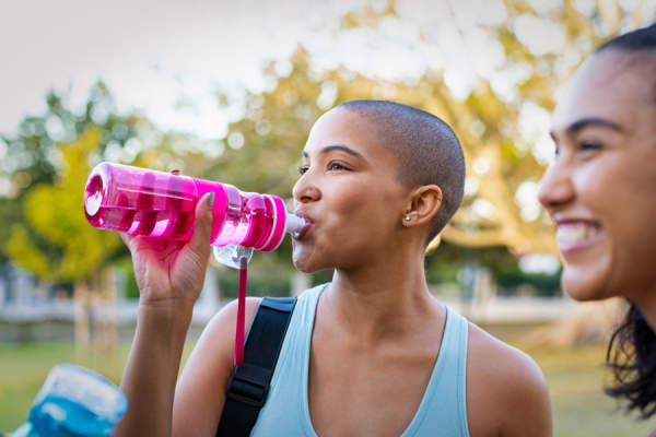 女子用剃光头喝粉红色的可重复使用的水瓶出来