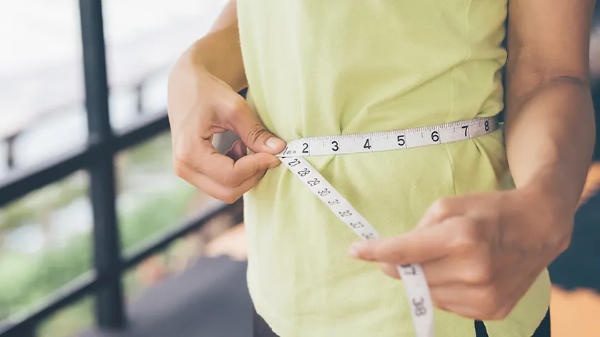 一位女士正在测量她的腰围，以计算她的相对脂肪量。