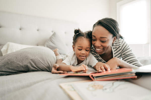 母亲和小女儿躺在家里的床上看故事书。