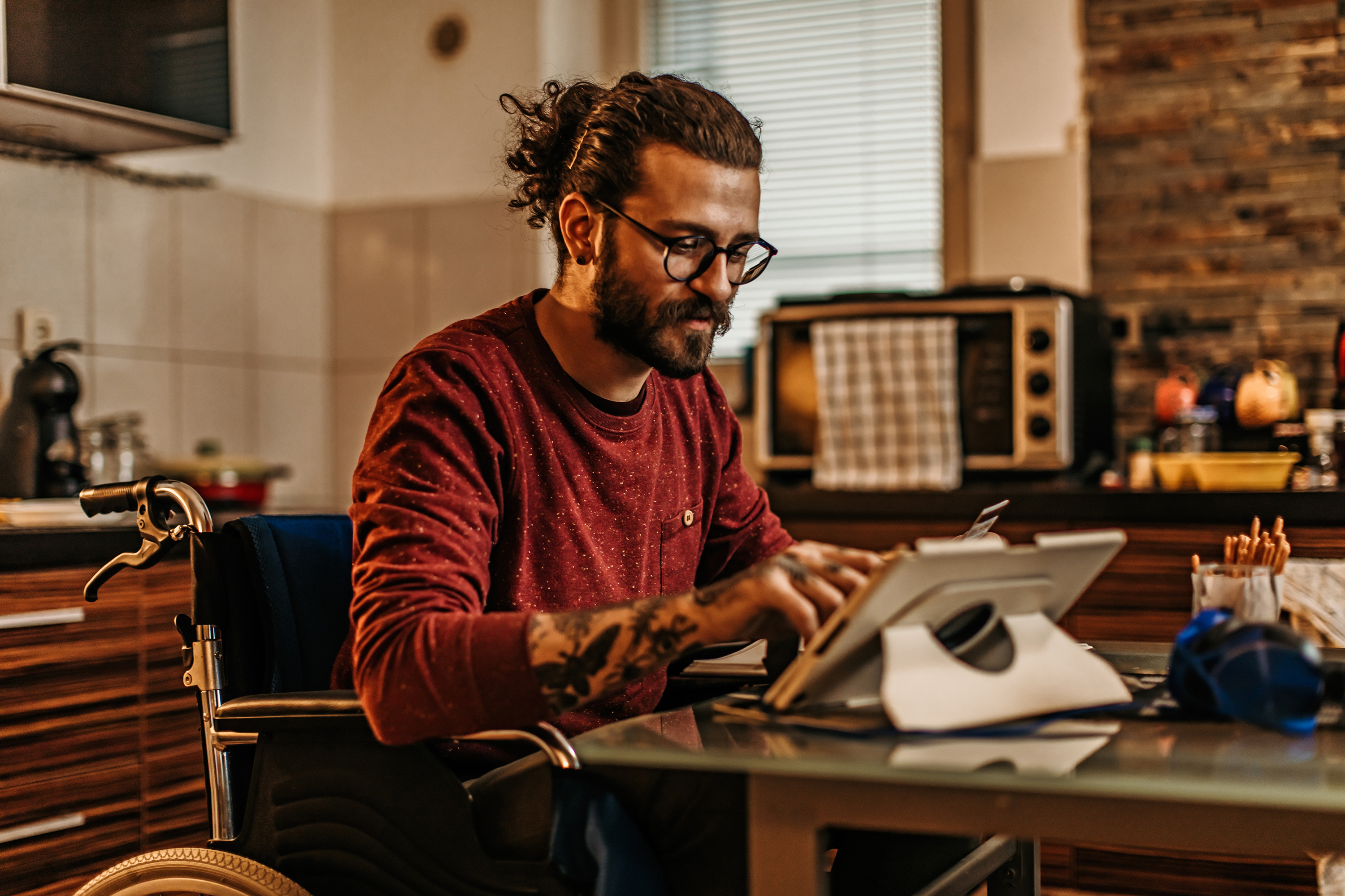 男人坐在轮椅上使用平板电脑在厨房里