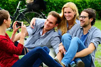 Woman taking a photo of a smiling group of friends on college campus.