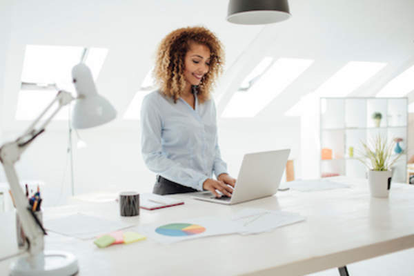 年轻女性在笔记本电脑上工作,站在实验室的桌子旁,在开放的家庭办公环境中。