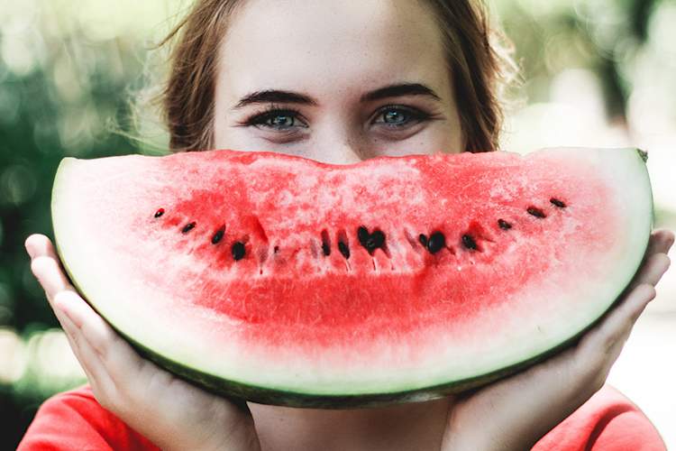 快乐的年轻女子背后的西瓜片微笑。