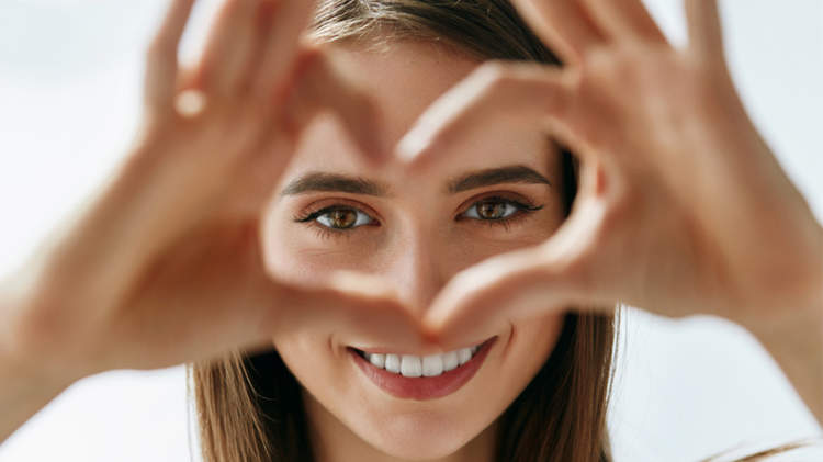 年轻的微笑着的女人用手在眼睛周围做一个心形。