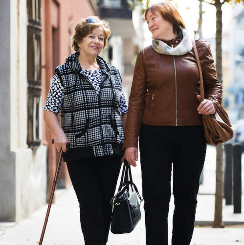 两名老年妇女在人行道上走在一起。