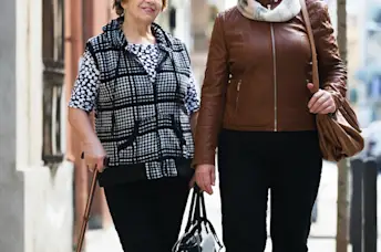 Two older women walking together on the sidewalk.