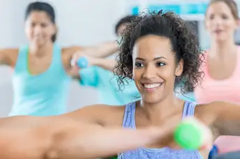 Smiling woman in group exercise class with hand weights.