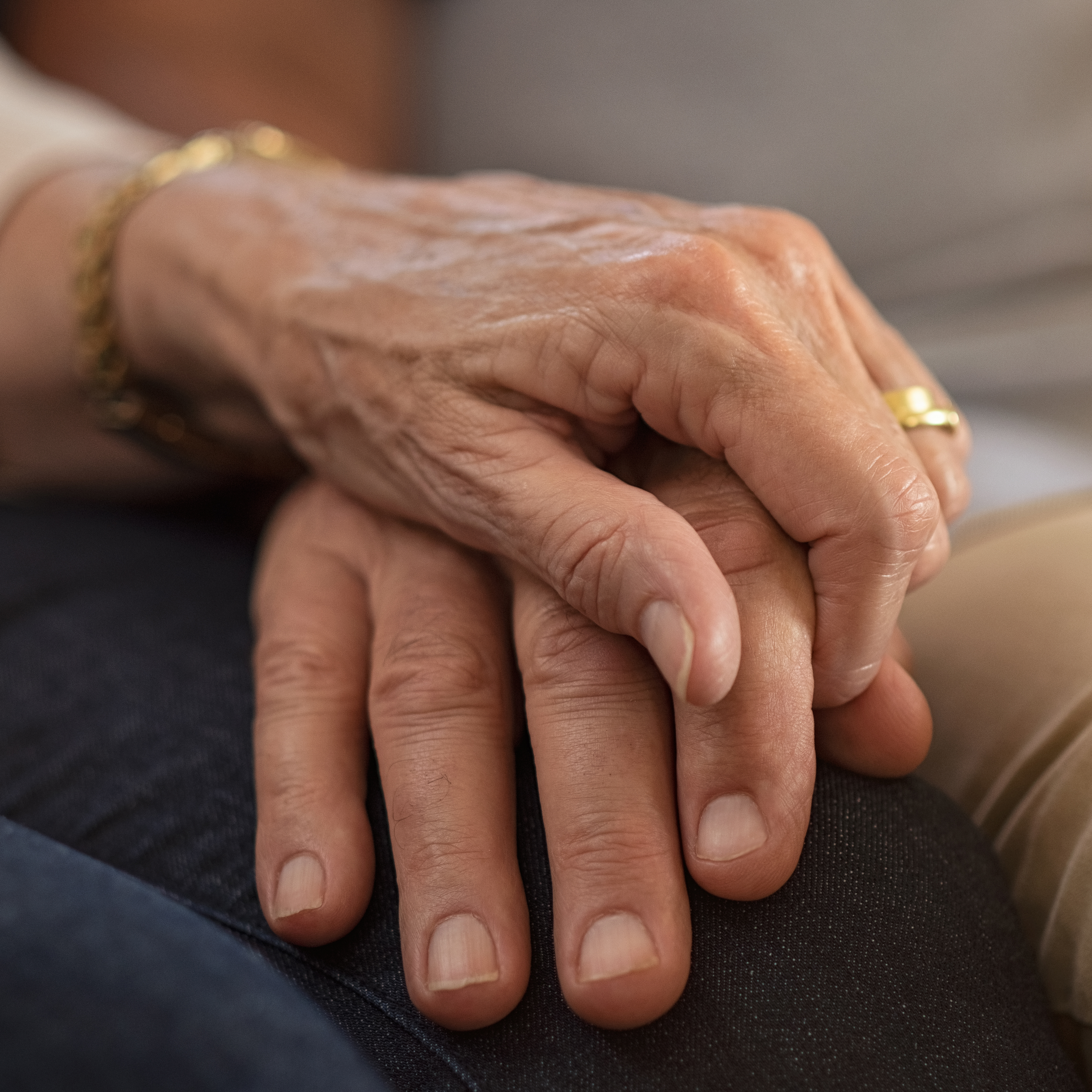 老年夫妇坐在沙发上手牵着手的特写镜头。