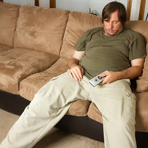 懒惰的男人睡着用遥控在手上在沙发上。