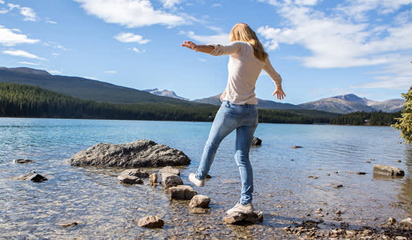 年轻女子在水中从一块石头走到另一块石头。