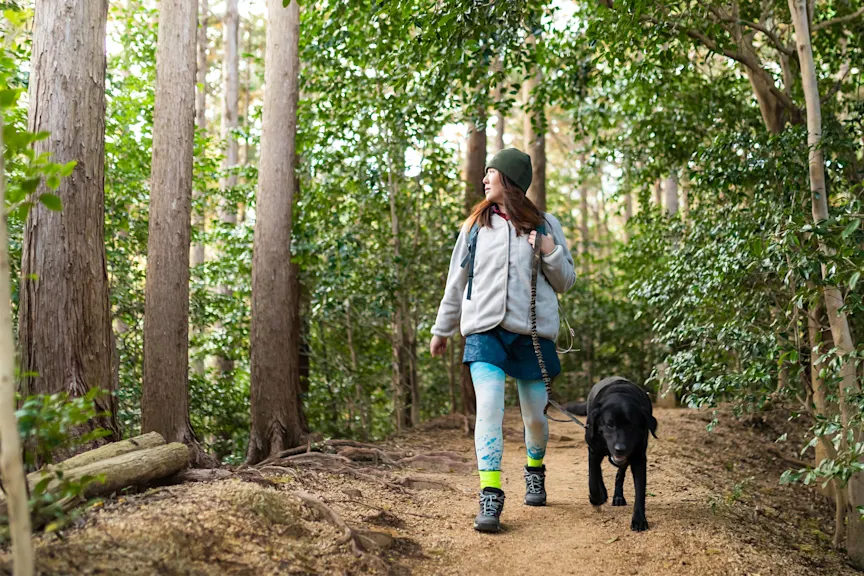 A woman hikes in the woods with her dog