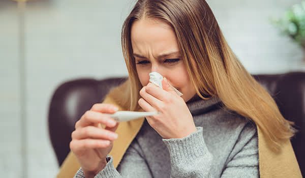 患流感的妇女一边擤鼻子一边测体温。