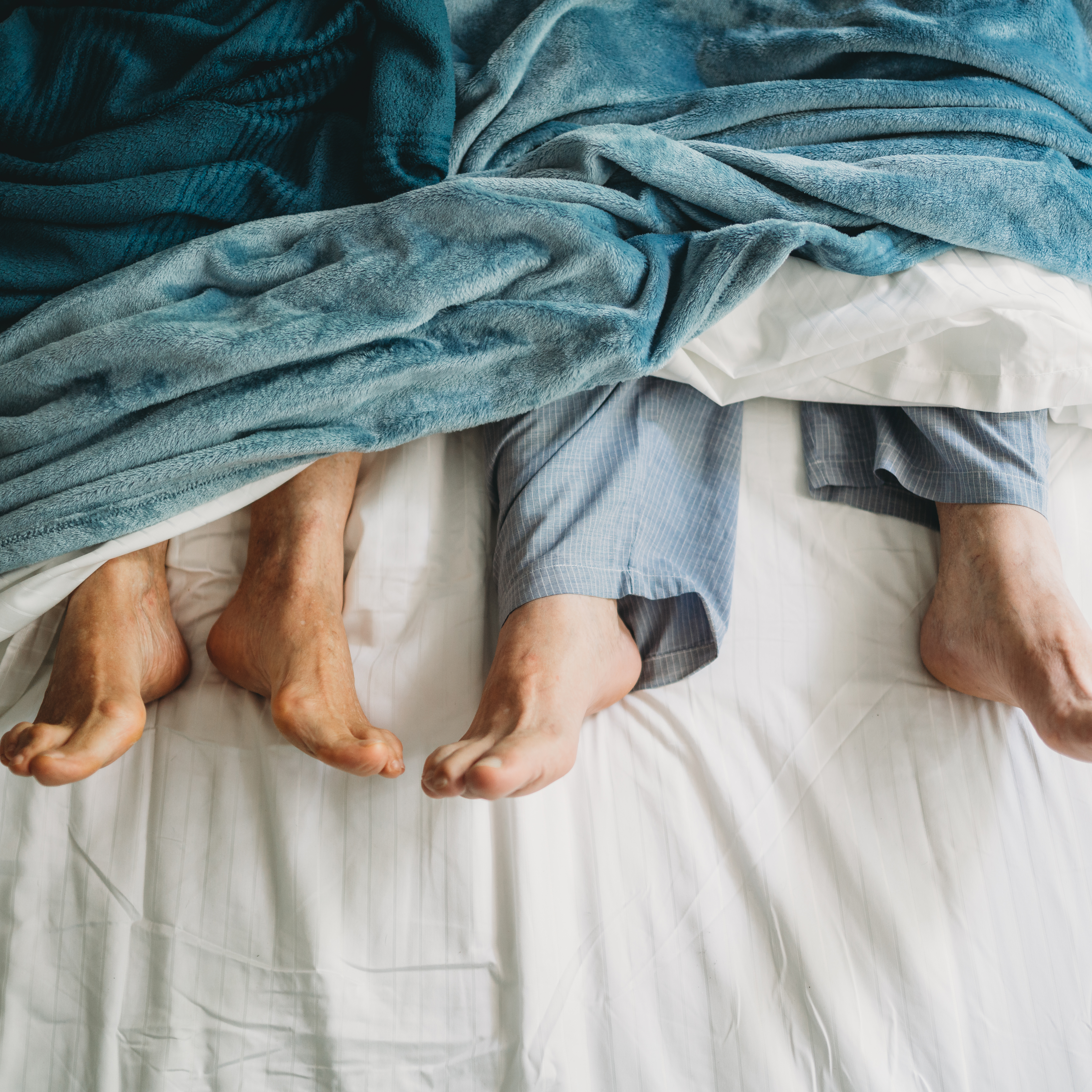 一对夫妻躺在床上，他们的脚从床单下伸出来。