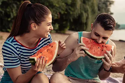 一对年轻夫妇在海滩上吃西瓜。
