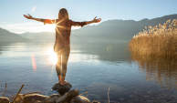 一个女人站在一块岩石上与伸开双臂湖。