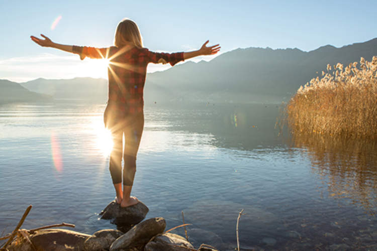 一个女人站在一块岩石上与伸开双臂湖。