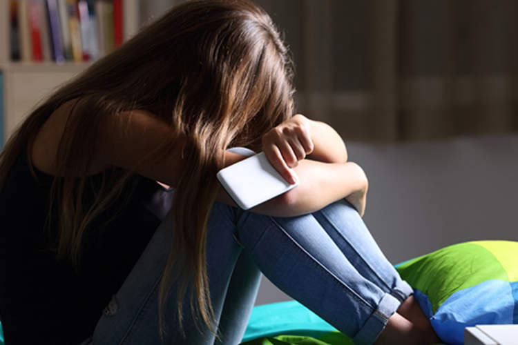 悲伤的年轻女孩在她的头部朝下,手机在手床上。