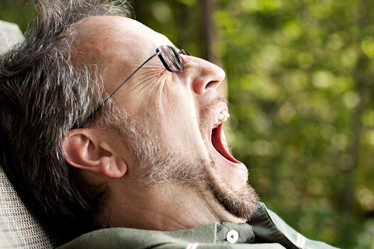 一个男人坐在屋外的草坪躺椅上打哈欠。