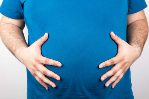 Man in blue t-shirt holding  his large belly.