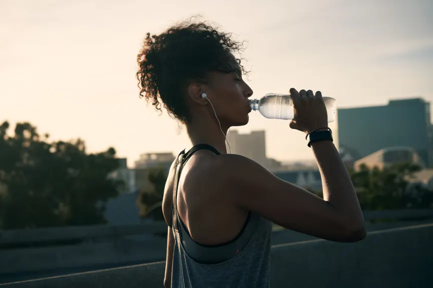 早上在城市跑步后，一名戴着耳机和饮用水的有吸引力的年轻女子的裁剪镜头