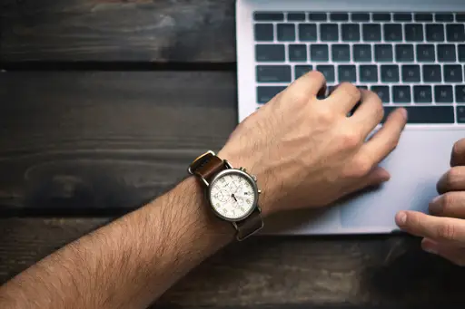 男人在笔记本电脑上打字，看着手表